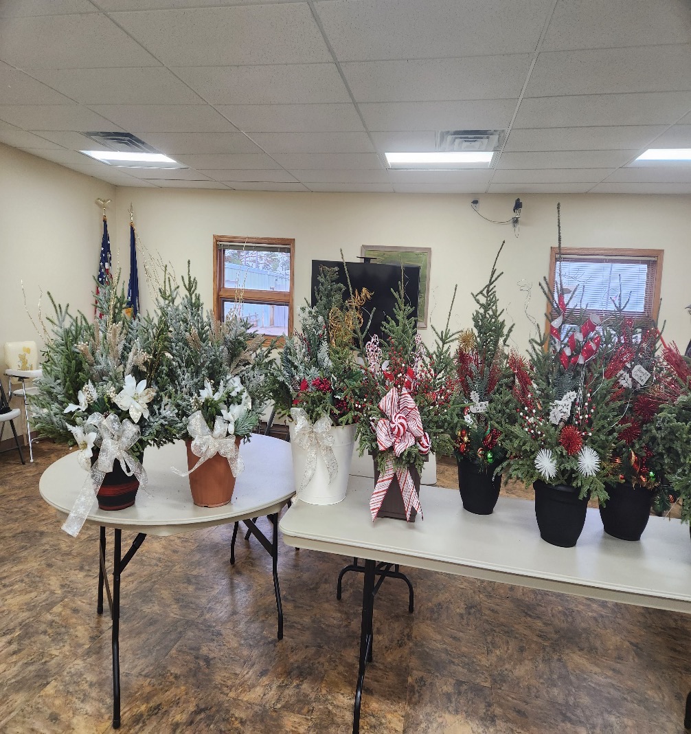 Holiday planters filled with evergreen boughs, ribbons and bows lined up on tables at Dodge City Hall