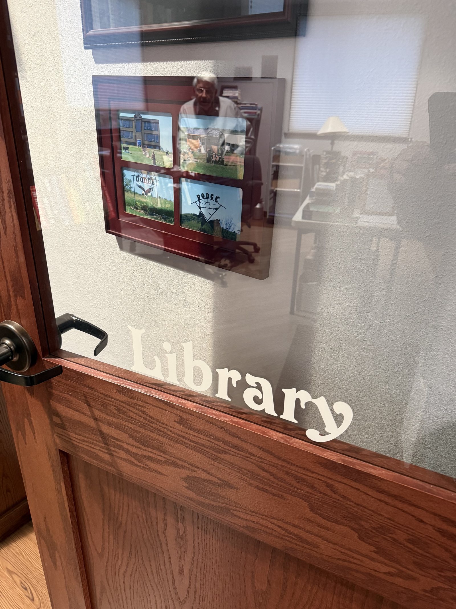 The glass door marked Library inside Dodge City Hall, with a framed welcome notice and a display of Dodge photographs on the wall behind it